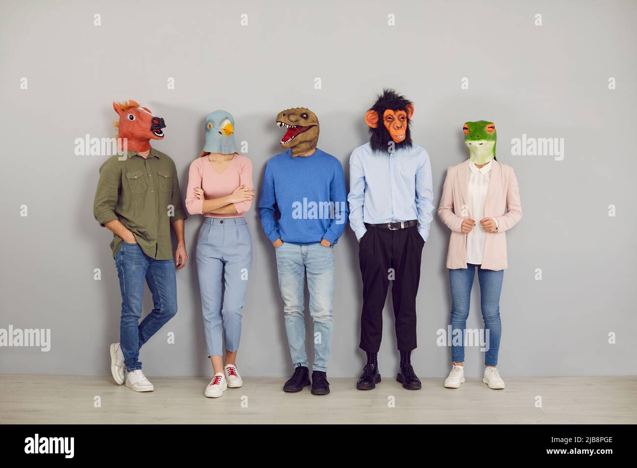Eine Gruppe von Menschen, die komische, absurde Tiermasken tragen und an der Bürowand stehen Stockfoto