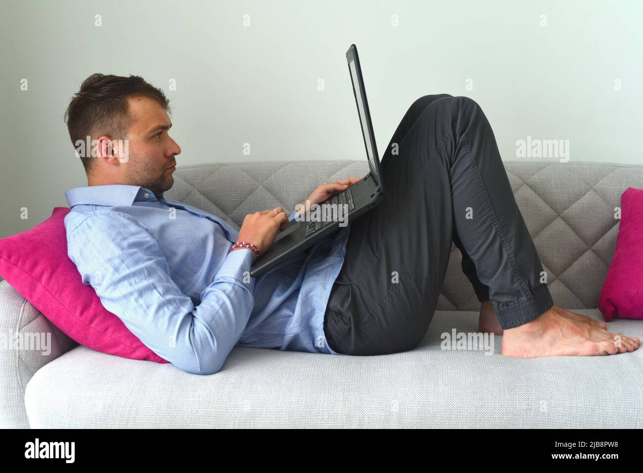 Junger freiberuflicher Mann, der von zu Hause aus mit seinem Laptop auf der Couch arbeitet Stockfoto