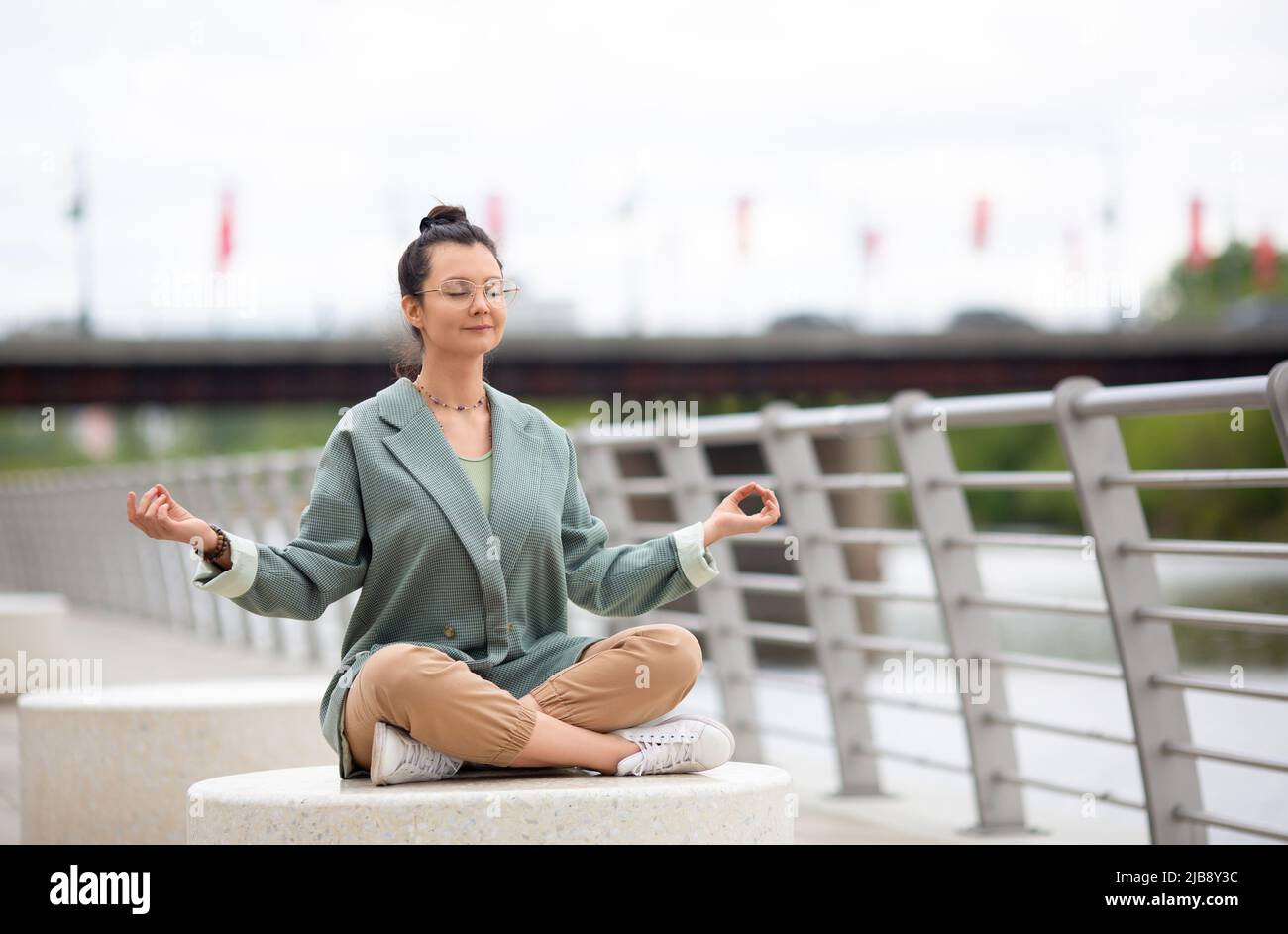 Foto einer Frau, die auf dem Damm meditiert. Sie ruht sich aus vom Bürolärm und dem Lärm der Stadt. Digitales Detox-Konzept. Stockfoto