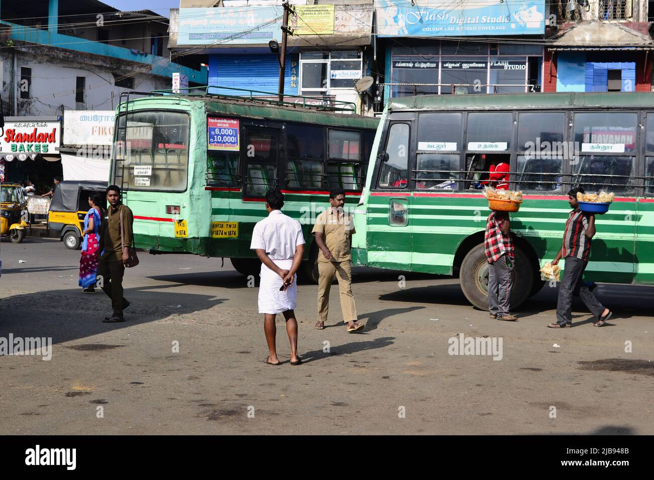 Sultan Bathery, Indien - Januar, 2017: Alte grüne indische Busse warten am Busbahnhof auf Fahrgäste. Männer mit Körben verkaufen Snacks an Busreisende Stockfoto