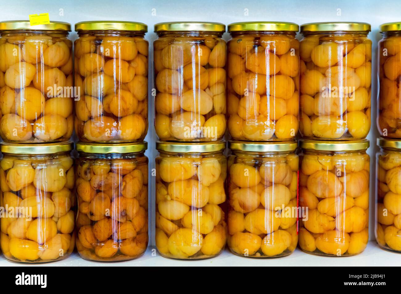 Sogar Reihen von Dosen mit Kastanien in goldenem Sirup mit gelben Deckeln in einem transparenten Glasglas Stockfoto