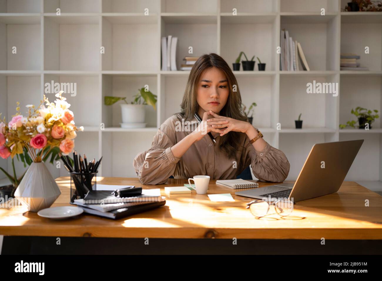Durchdachte Geschäftsfrau, die an ihrem Arbeitsplatz sitzt und über die Lösung des Projektproblems nachdenkt. Stockfoto