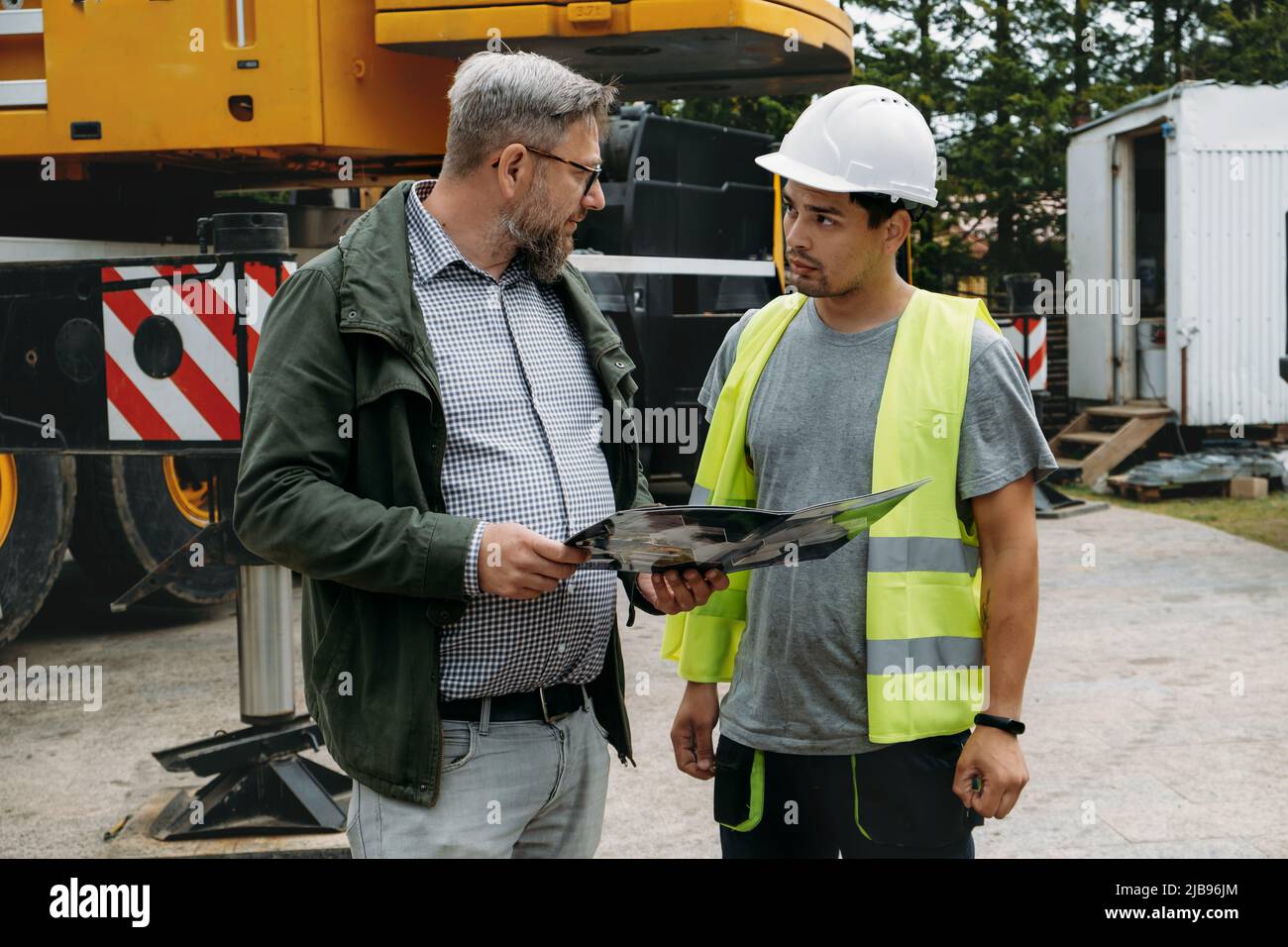 Vorarbeiter und Kunde oder Kunde stimmen über zukünftige Bauarbeiten auf der Baustelle überein. Architekt diskutiert Projekt mit dem Baumeister über Kranfahrzeug Stockfoto