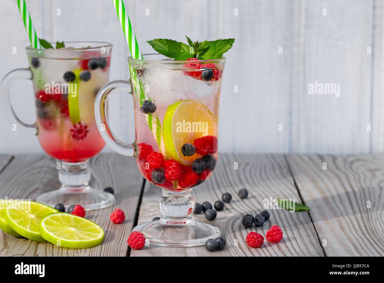 Frische hausgemachte Sommercocktails mit Eis, Limette und Beeren in Gläsern mit Stroh, Copyspace. Stockfoto