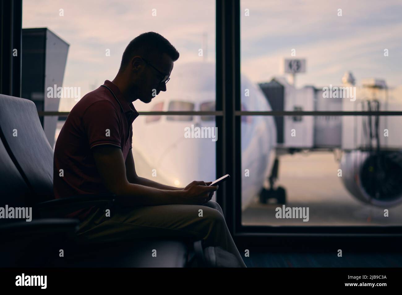 Silhouette eines jungen Mannes, der auf den Flug wartet. Reisende, die am Flughafenterminal telefonieren. Stockfoto