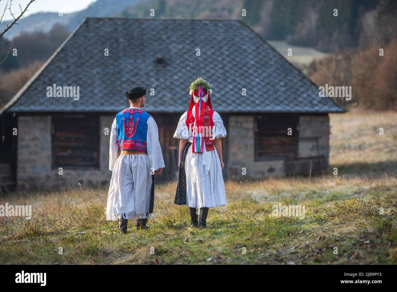 Ein Paar in traditioneller Tracht. Slowakische Kostüm im Herbst Natur. Altes Landhaus im Hintergrund. Junges Paar in Tracht Wal Stockfoto