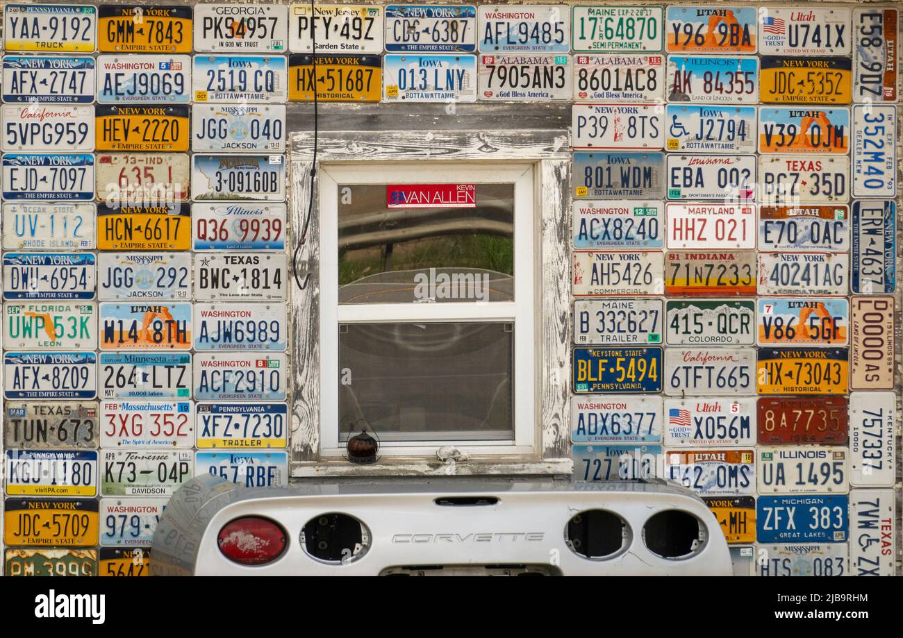 Autokennzeichen aus verschiedenen Staaten und ein Korvettenwagen hinten unter einem Fenster an der Seite eines Gebäudes in Mount Morris NY Stockfoto