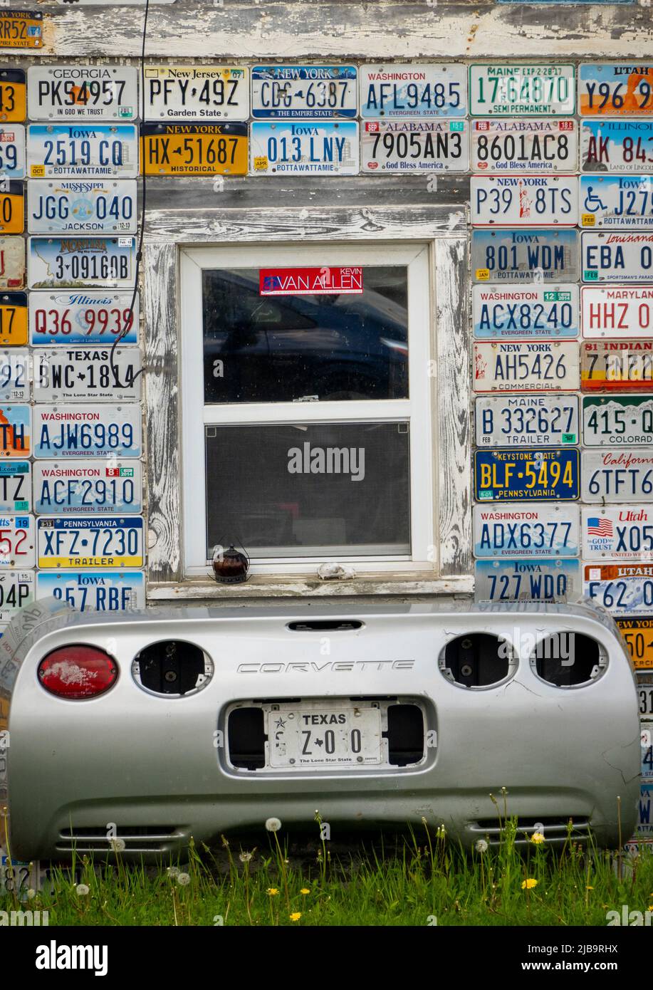 Autokennzeichen aus verschiedenen Staaten und ein Korvettenwagen hinten unter einem Fenster an der Seite eines Gebäudes in Mount Morris NY Stockfoto