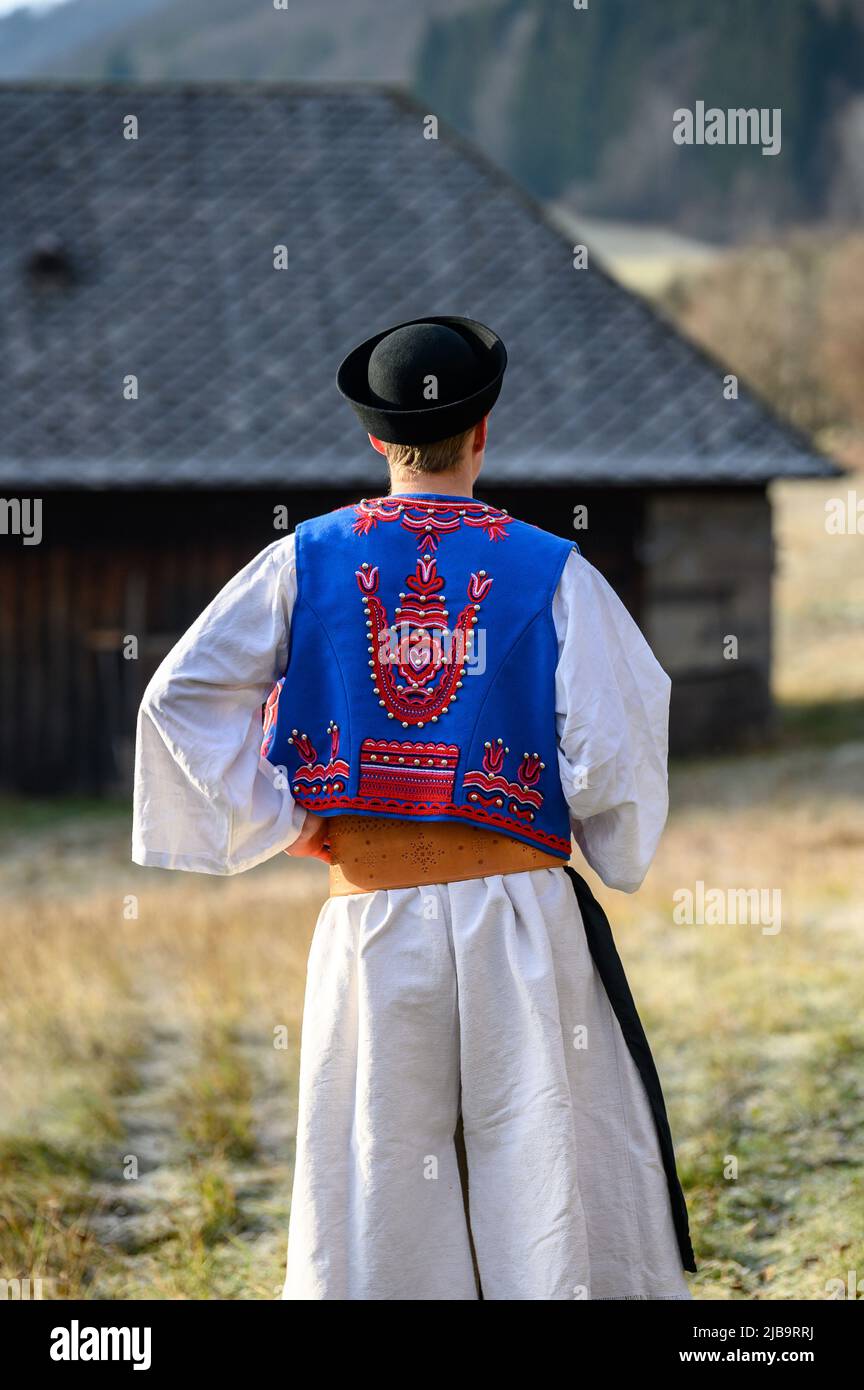 Ein Mann in traditioneller Tracht. Slowakische Kostüm im Herbst Natur. Altes Landhaus im Hintergrund. Details des slowakischen Kostüms von De Stockfoto
