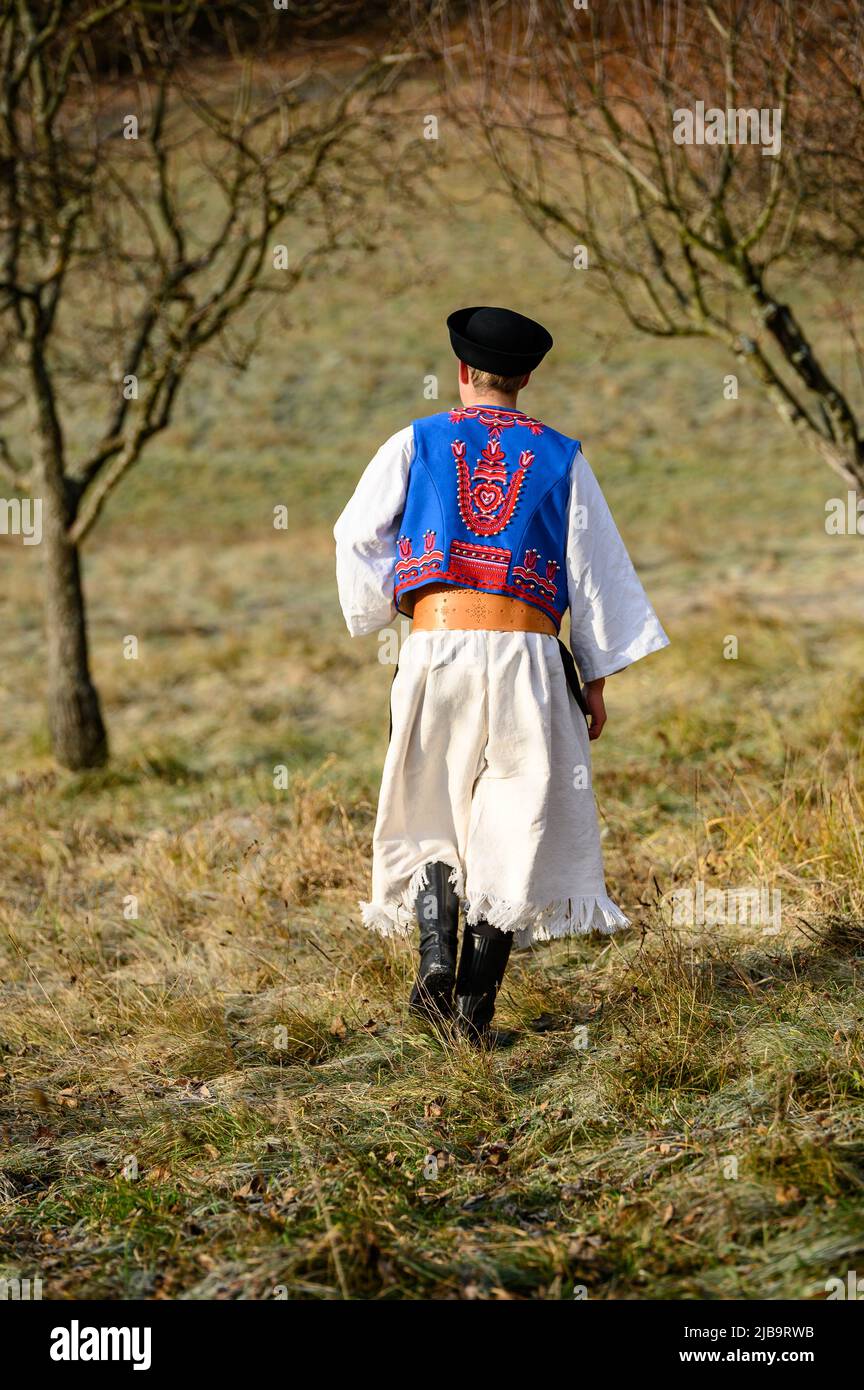 Ein Mann in traditioneller Tracht. Slowakische Kostüm im Herbst Natur. Altes Landhaus im Hintergrund. Details des slowakischen Kostüms von De Stockfoto