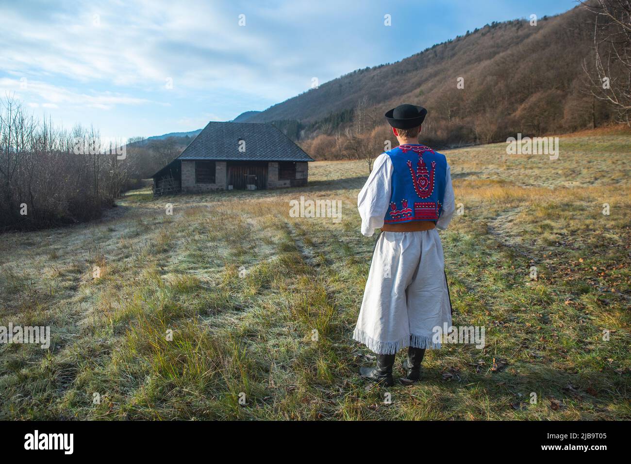 Ein Mann in traditioneller Tracht. Slowakische Kostüm im Herbst Natur. Altes Landhaus im Hintergrund. Details des slowakischen Kostüms von De Stockfoto