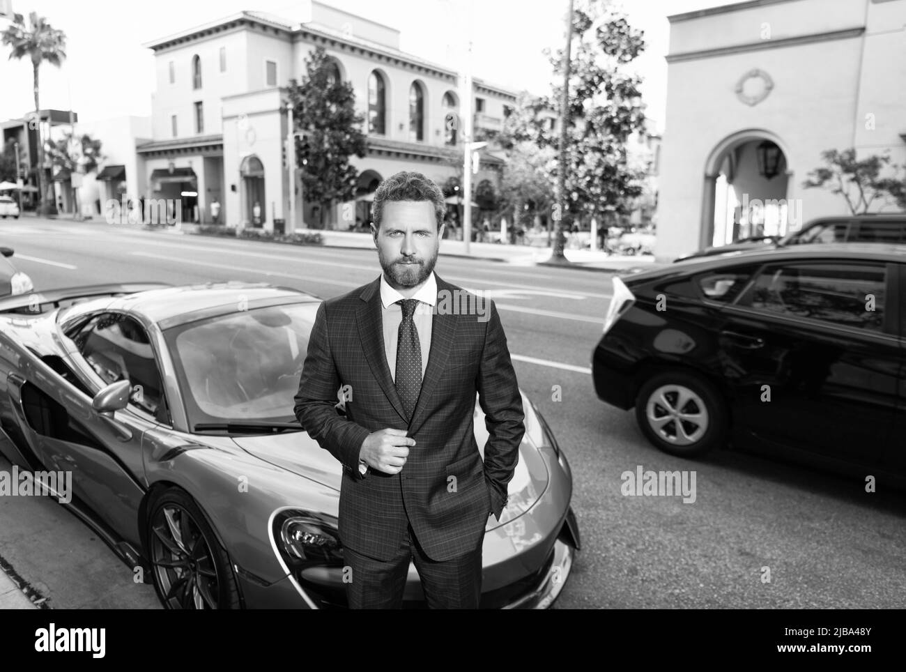 Reifer bärtiger Geschäftsmann in teuren Anzug in der Nähe von Auto Outdoor, Geschäftserfolg Stockfoto