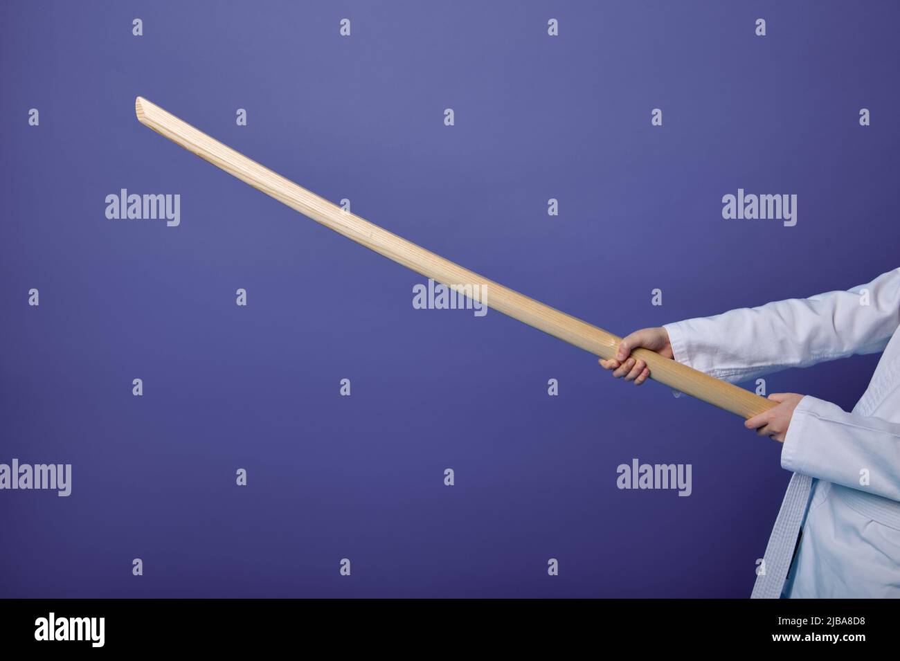 Beschnittene Ansicht der Hände des Aikido-Kämpfers mit Holzwaffe - Schwert-Bokken - beim Üben orientalischer Kampfkünste auf violettem Hintergrund mit Stockfoto