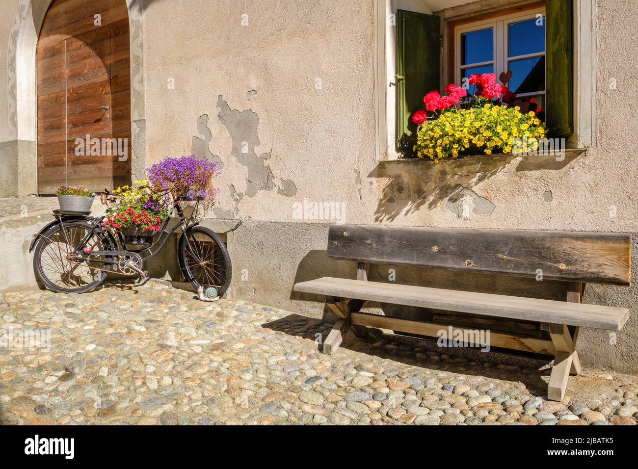 Ein altes rostiges Fahrrad, dekoriert mit wunderschönen Blumen, im historischen Dorfzentrum von S-chanf (Oberes Engadine-Tal, Grisons, Schweiz) Stockfoto