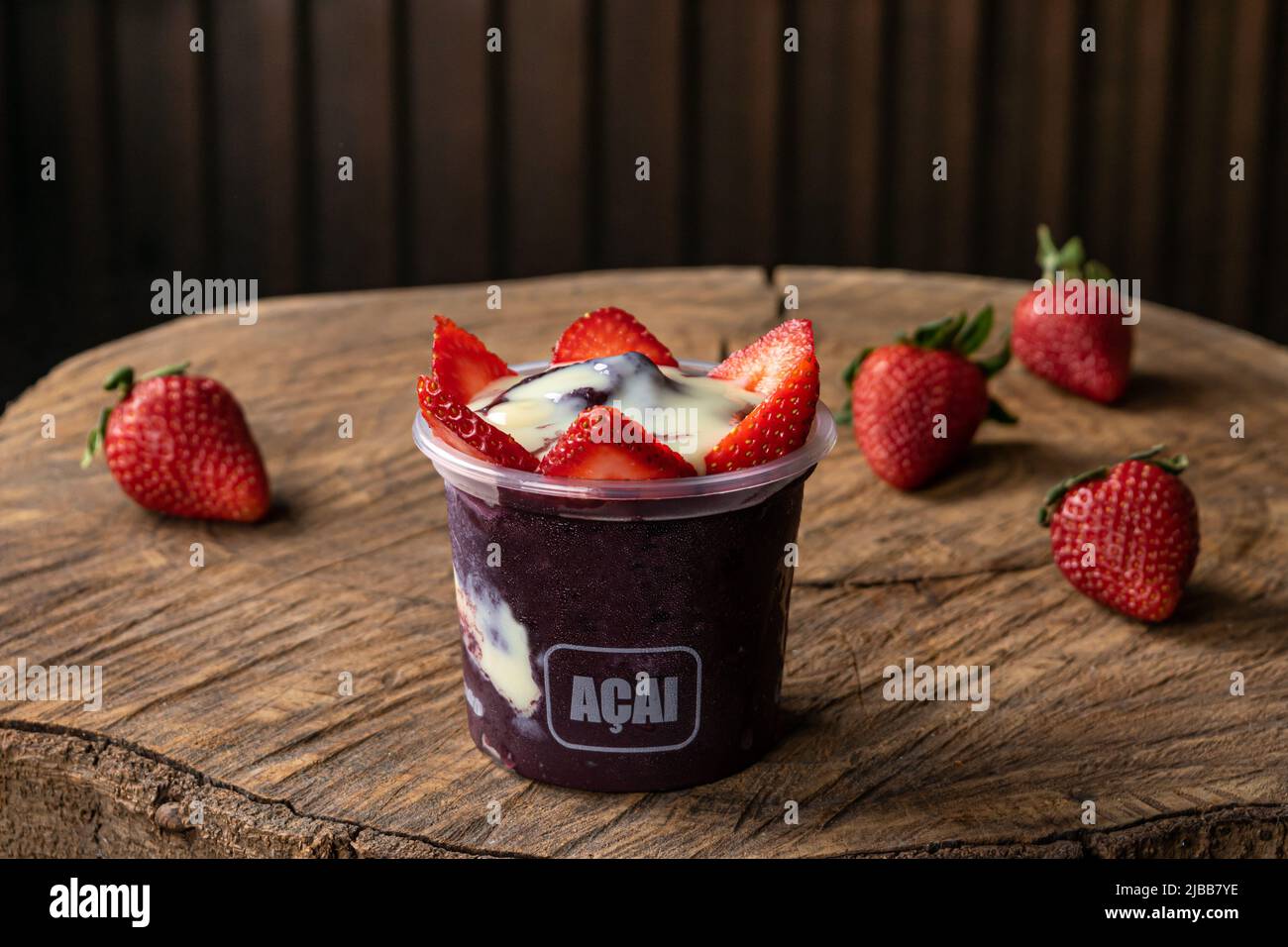 Köstliche brasilianische Açaí-Creme, in einem Plastikbecher mit Erdbeer-Topping, auf einem rustikalen Holzhintergrund. Sommer acai Smoothie Stockfoto