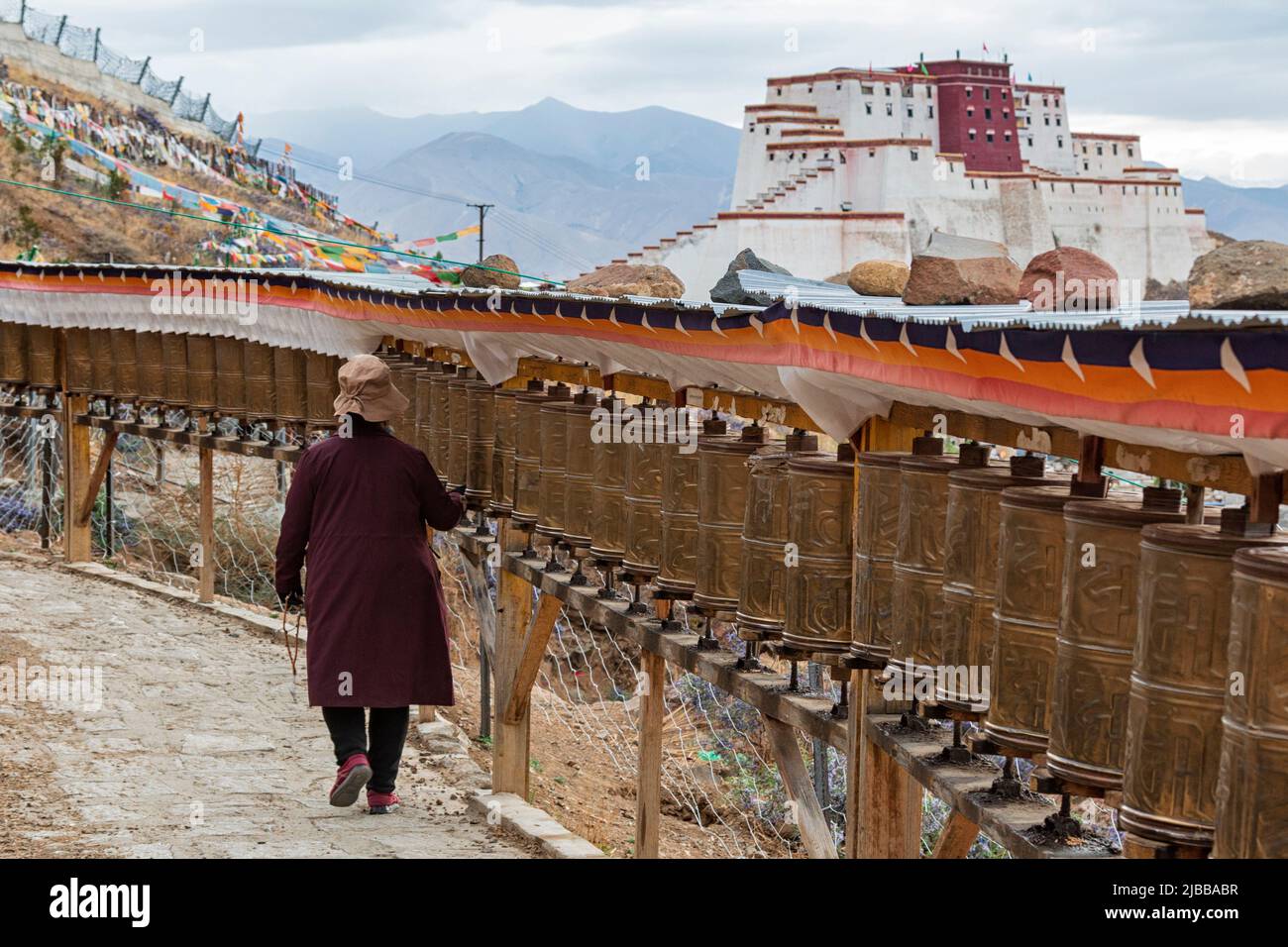 Tibetischer Pilger, der eine Kora um das Kloster Tashilumpo mit dem kleinen Potala Palast im Hintergrund durchführt Stockfoto