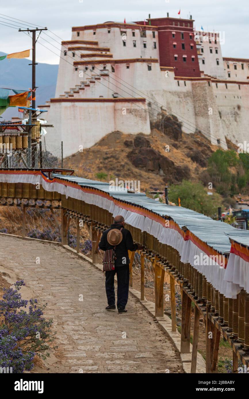Tibetische Pilger, die eine Kora um das Kloster Tashilumpo mit dem kleinen Potala Palast im Hintergrund durchführen Stockfoto