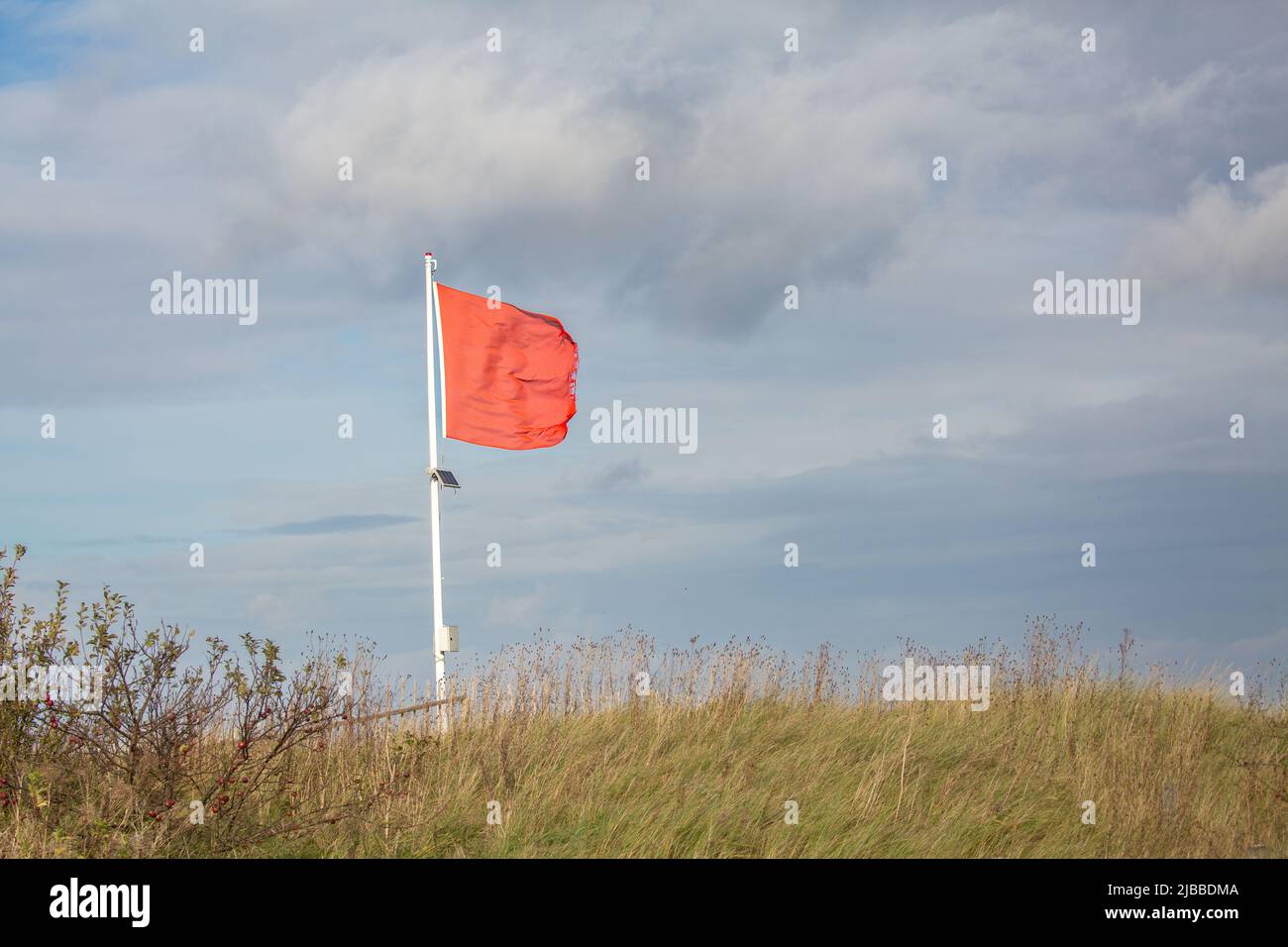 Rote Flagge winkt im Wind mit kleinem Solarpanel auf der Post am Norfolk Grass Beach in Großbritannien Stockfoto