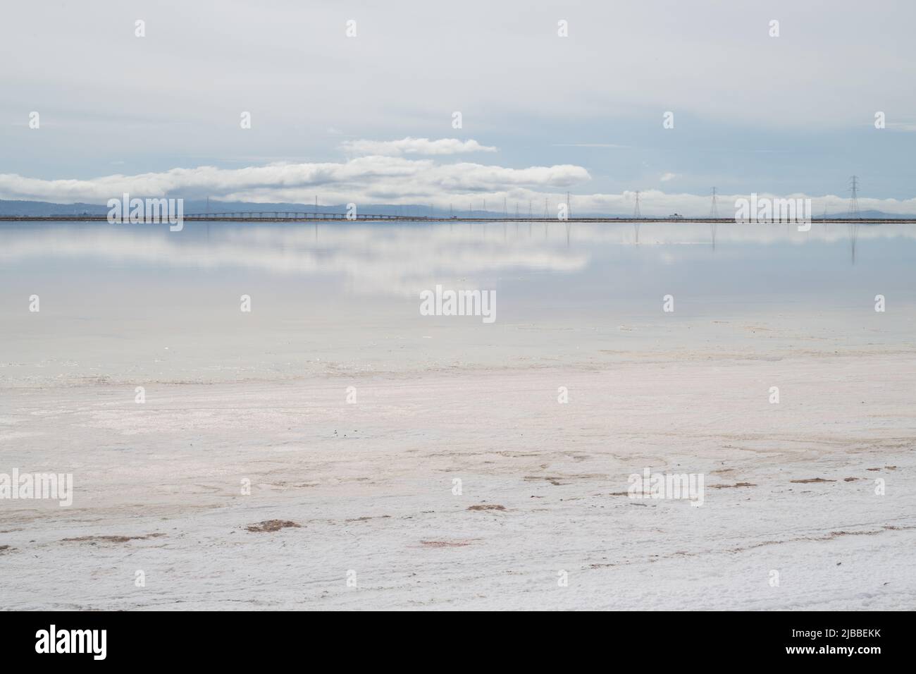 Das spiegelglatte Wasser von Salzverdampfungsteichen, das Wolken und Stromleitungen reflektiert. Stockfoto