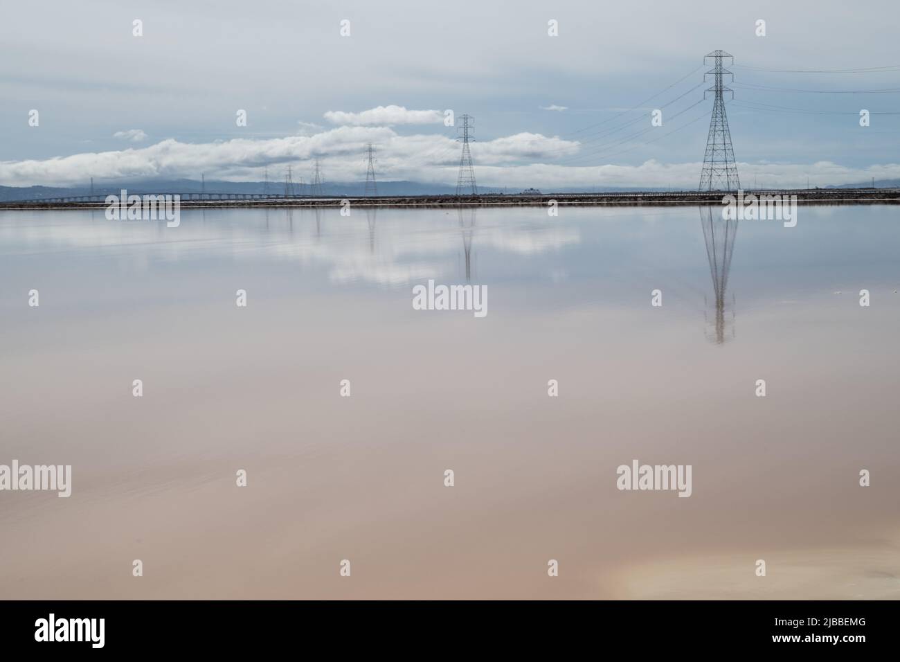 Das spiegelglatte Wasser von Salzverdampfungsteichen, das Wolken und Stromleitungen reflektiert. Stockfoto