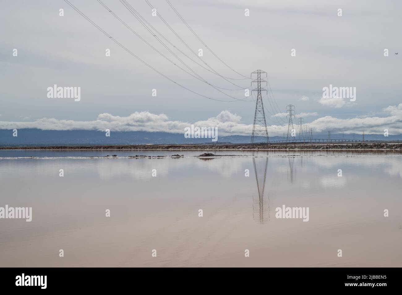 Das spiegelglatte Wasser von Salzverdampfungsteichen, das Wolken und Stromleitungen reflektiert. Stockfoto