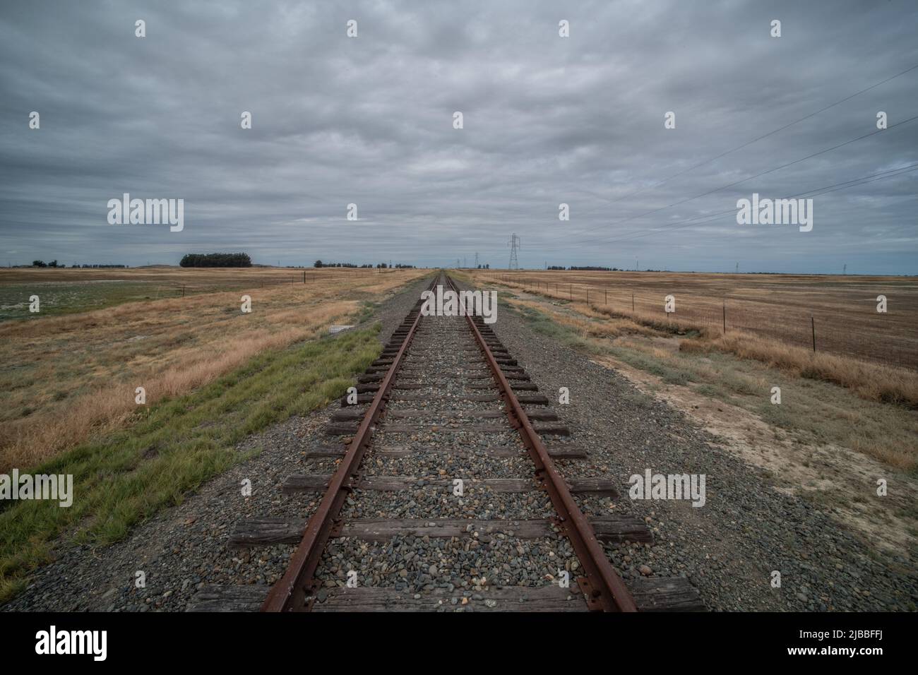 Eine Eisenbahn, die in die Ferne führt und am Horizont in flachem Grasland im Central Valley von Kalifornien, USA, verschwindet. Stockfoto