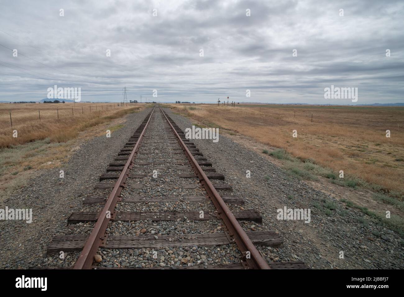 Eine Eisenbahn, die in die Ferne führt und am Horizont in flachem Grasland im Central Valley von Kalifornien, USA, verschwindet. Stockfoto