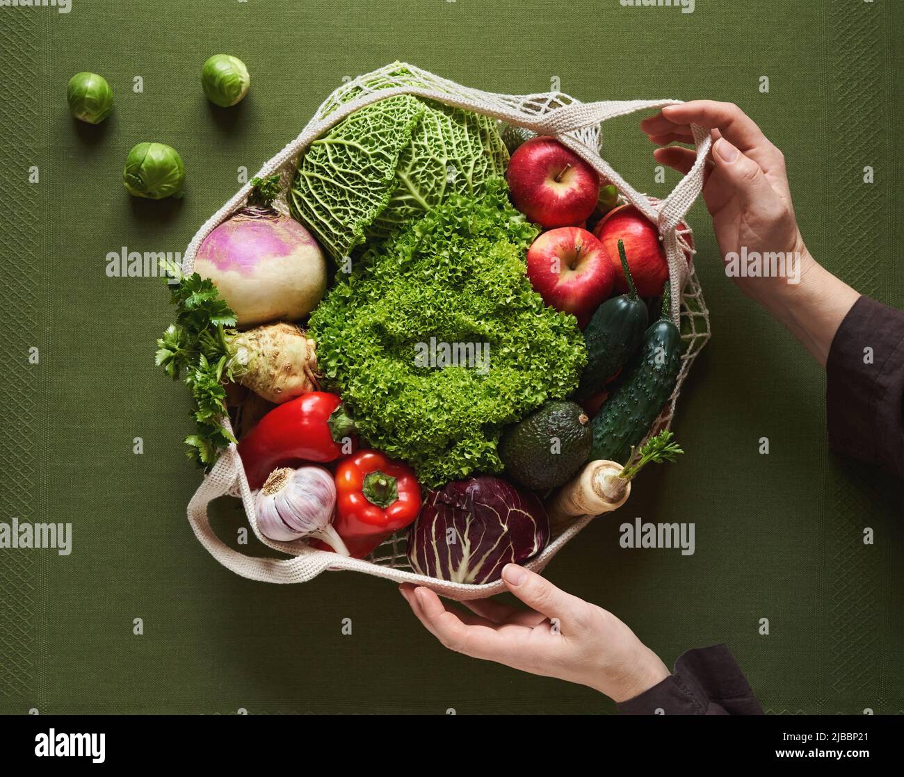 Frauenhände halten einen ökologischen Baumwollstring-Beutel mit frischem Obst und Gemüse auf grünem Hintergrund - Zero Waste Konzept Stockfoto