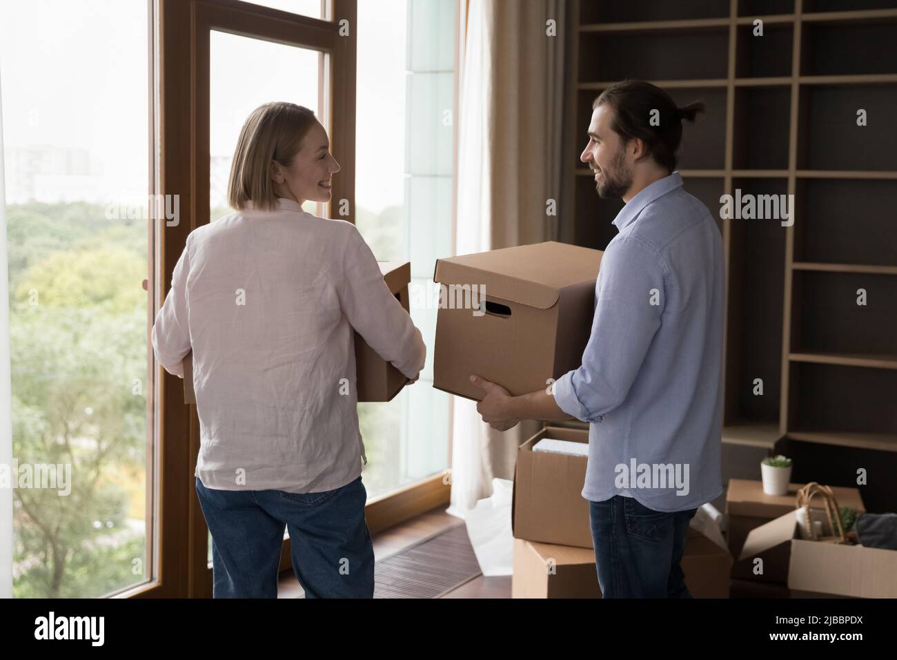 Paar, die bei einem Umzug Boxen mit Habseligkeiten ins Wohnzimmer tragen Stockfoto