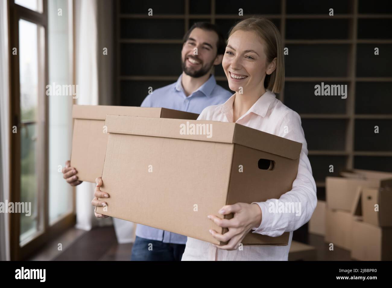 Pärchen, die Boxen mit Habseligkeiten in einem unmöblierten Wohnzimmer halten Stockfoto