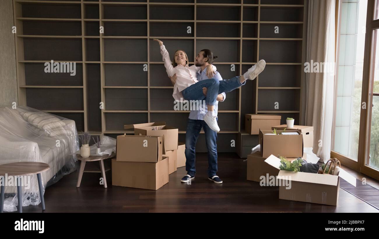 Ehemann auf Händen aufziehen Frau feiern Hauswarming im Wohnzimmer Stockfoto