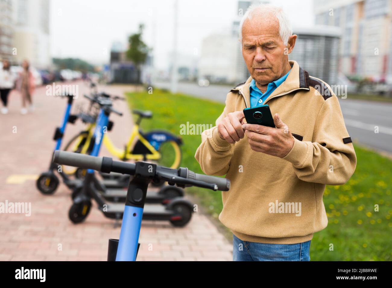 Älterer Mann mietet sich einen Elektroroller mit dem Mobiltelefon Stockfoto