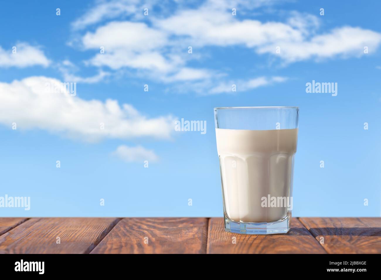 Milch im Glas auf dem Tisch mit blauem Himmel und Wolken auf dem Hintergrund Stockfoto