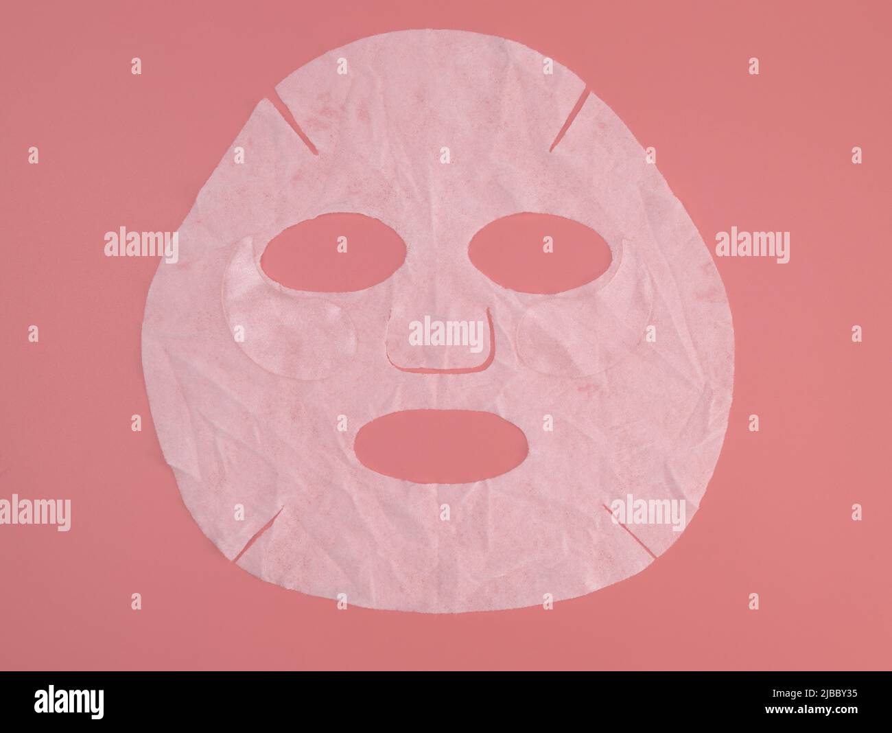 Blattmaske auf einem rosa Hintergrund Draufsicht. Hautpflege, Dermatologie, Beauty-Konzept. Trockene Textil-Gesichtsmaske flach Lay Mockup Stockfoto