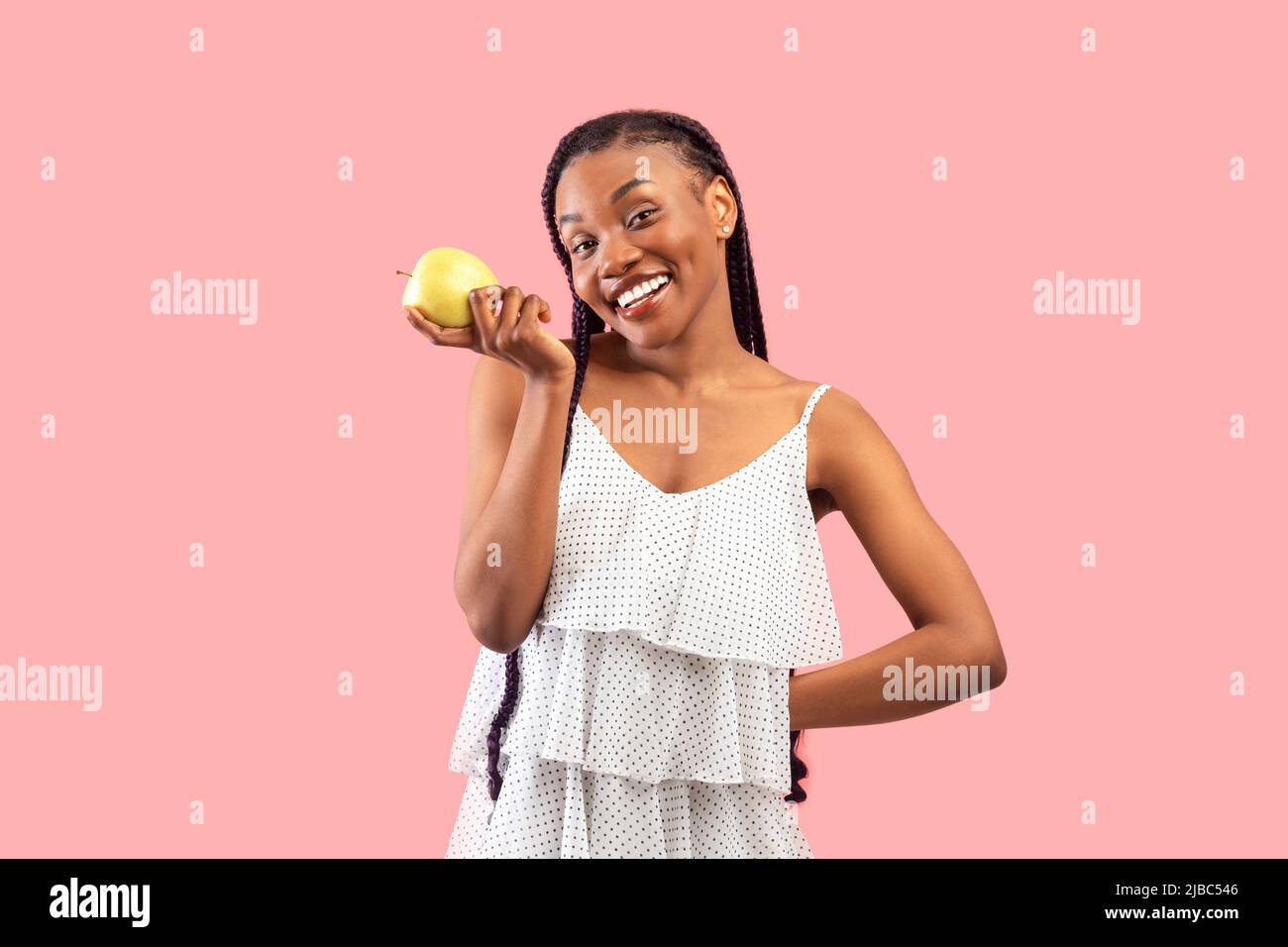 Junge afroamerikanische Frau hält Apfel auf rosa Studio-Hintergrund. Vitamine für gesunde Zähne und schöne Haut Stockfoto