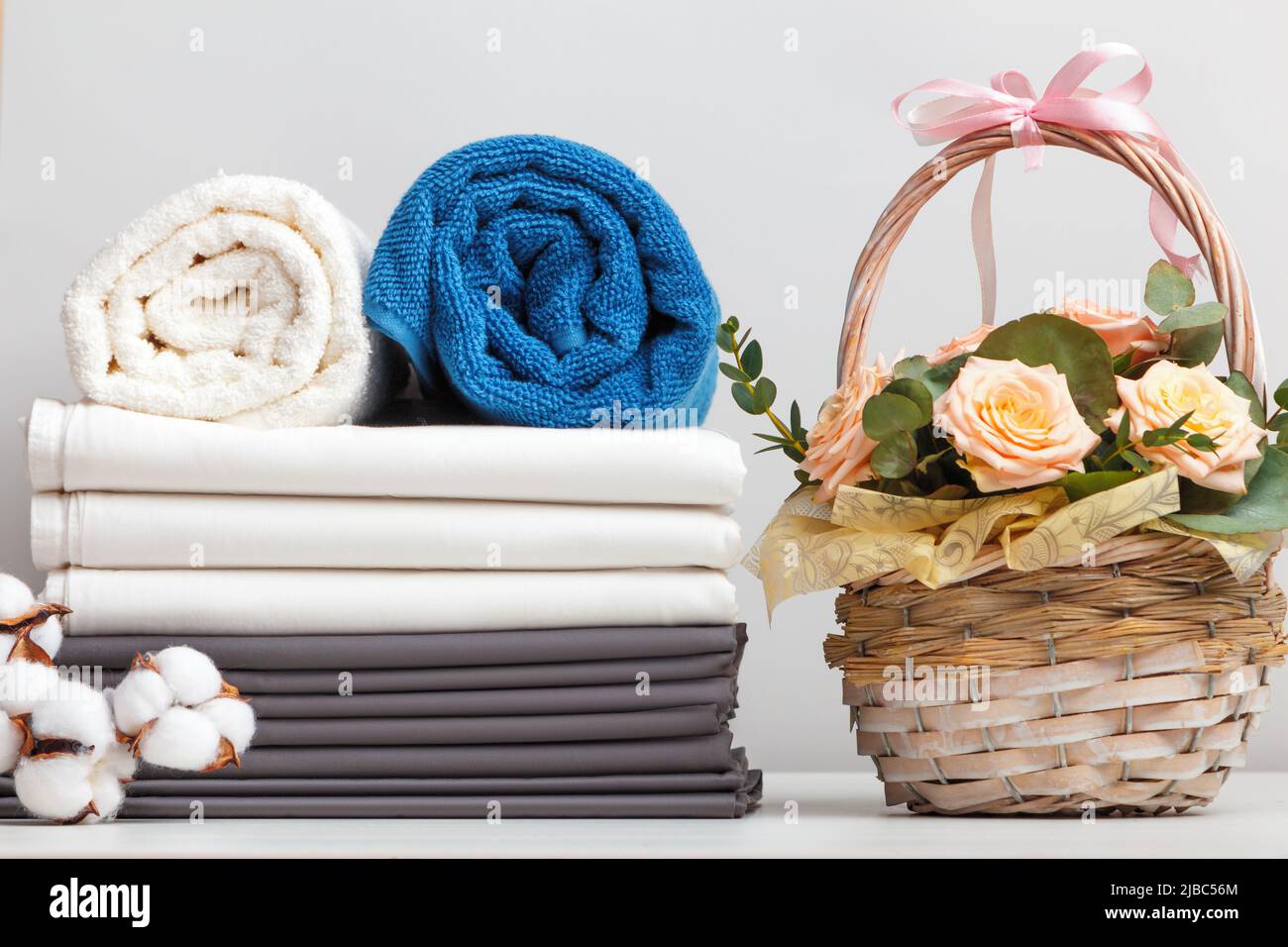 Ein Stapel Bettwäsche Bettwäsche Bettwäsche Brötchen mit Handtüchern. Korb mit Rosenblüten auf dem Tisch. Stockfoto