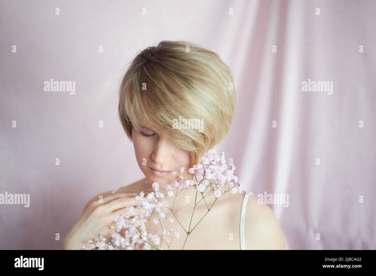 Porträt eines Mädchens auf einem rosa Hintergrund mit Blumen. Zärtlichkeit und feminin. Die Sphäre der Schönheit und der Gesundheit der Frauen. Kurzer Haarschnitt, blondes Haar Stockfoto