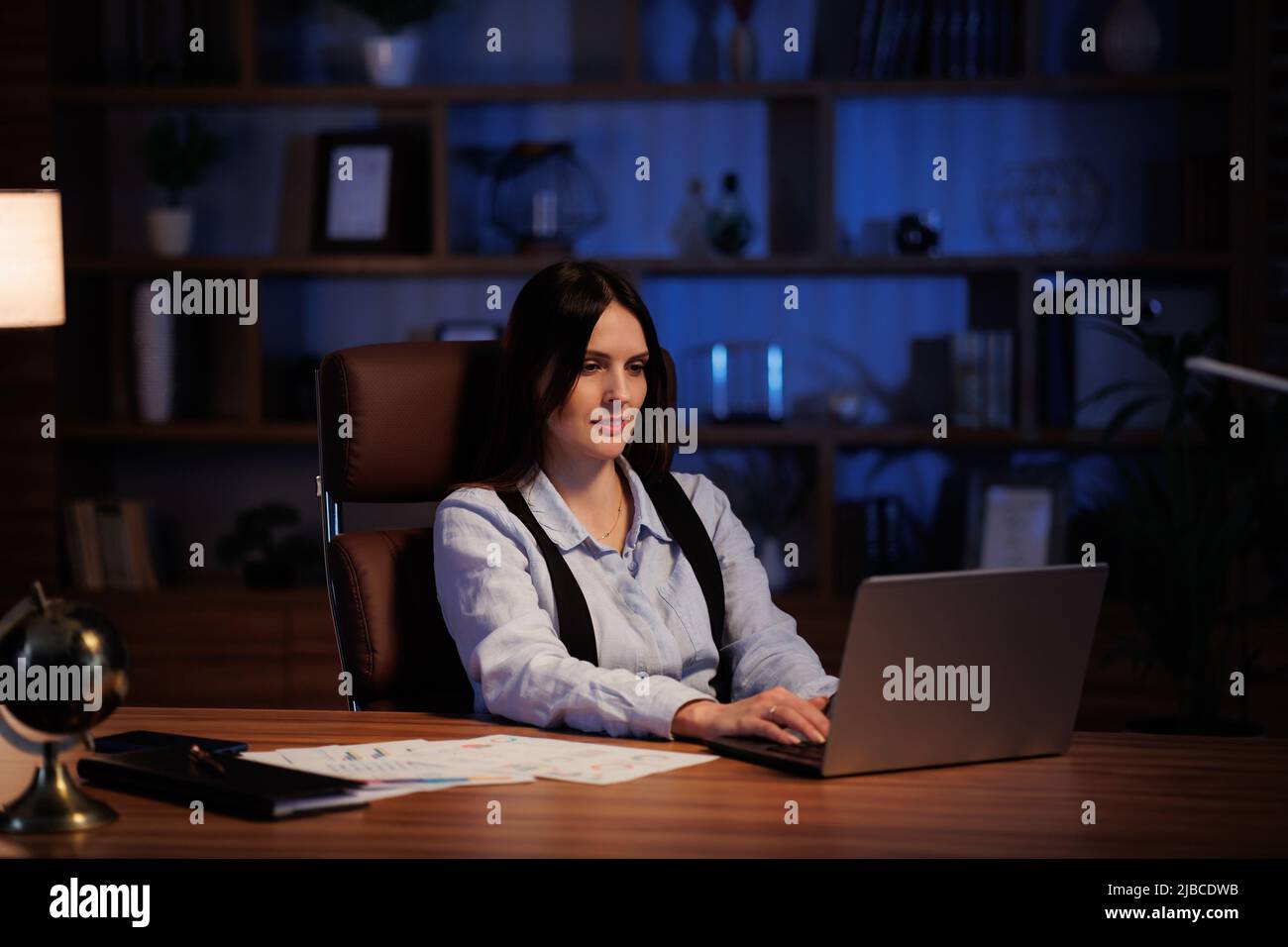 Junge Frau, die im Büro mit einem Laptop arbeitet. Büroangestellte analysieren Diagramme und Diagramme, arbeiten bis spät im Büro. Filmischer Seufzer Stockfoto