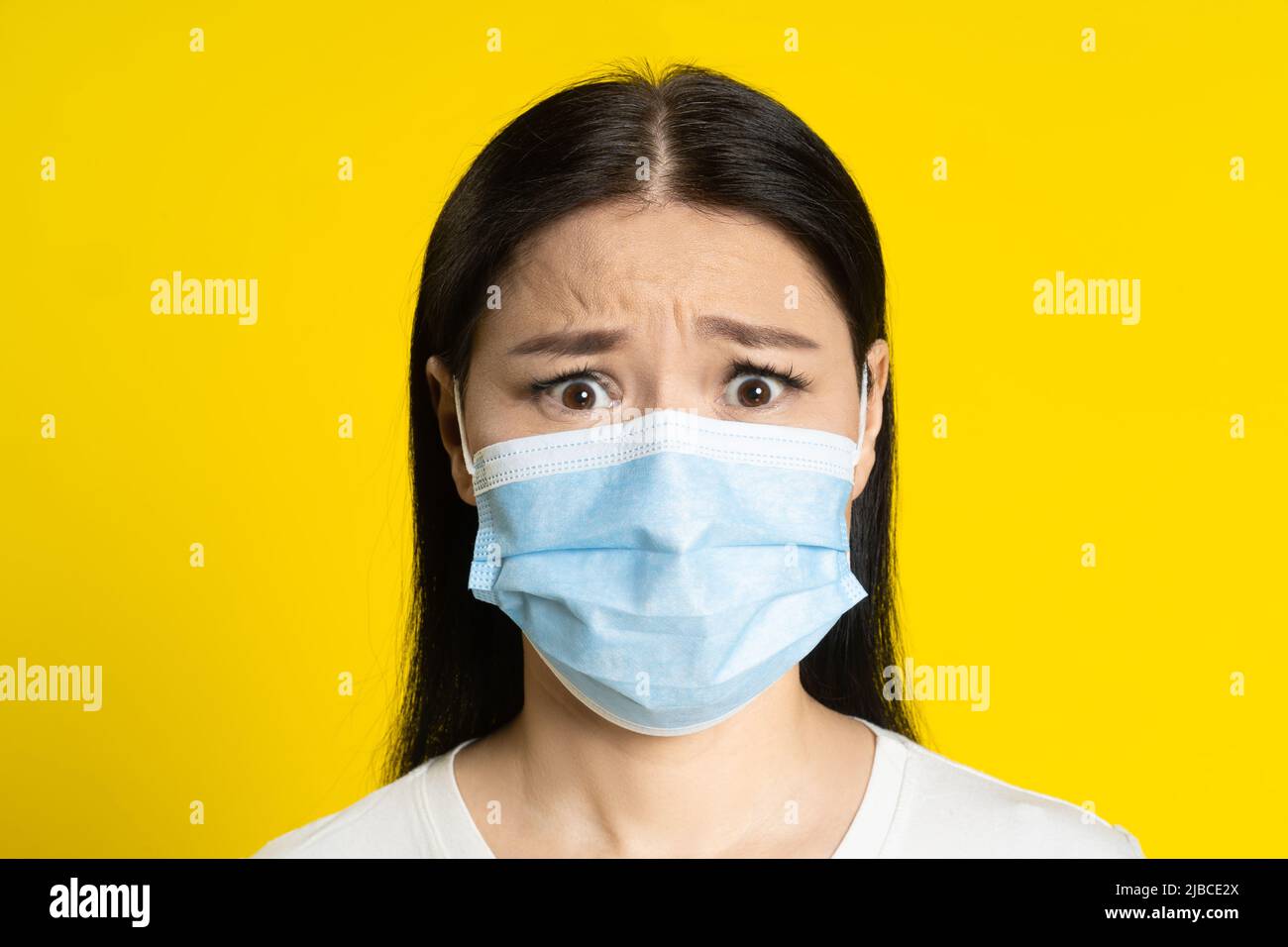 Angst vor Pandemie reife asiatische Frau trägt medizinische Gesichtsmaske Coronavirus oder Monkeypox Prävention. Charmante Frau mittleren Alters in weißem T-Shirt und medizinische Maske auf gelbem Hintergrund. Stockfoto