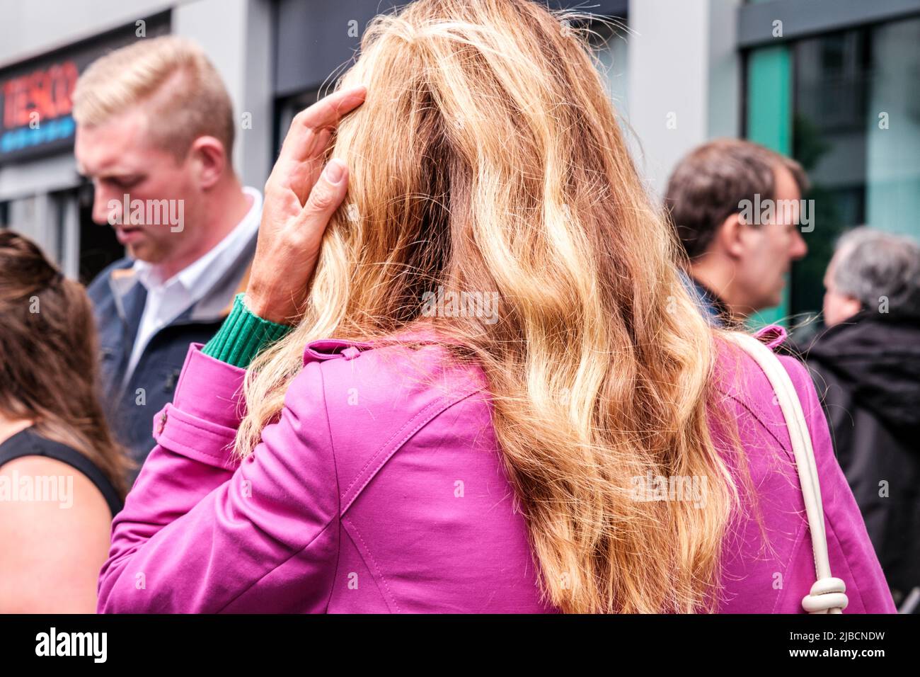 Epsom Surrey, London, Großbritannien, 04 2022. Juni, Frau mit langem blondem Haar gegen Eine rosa Jacke, die in einer Menschenmenge läuft Stockfoto