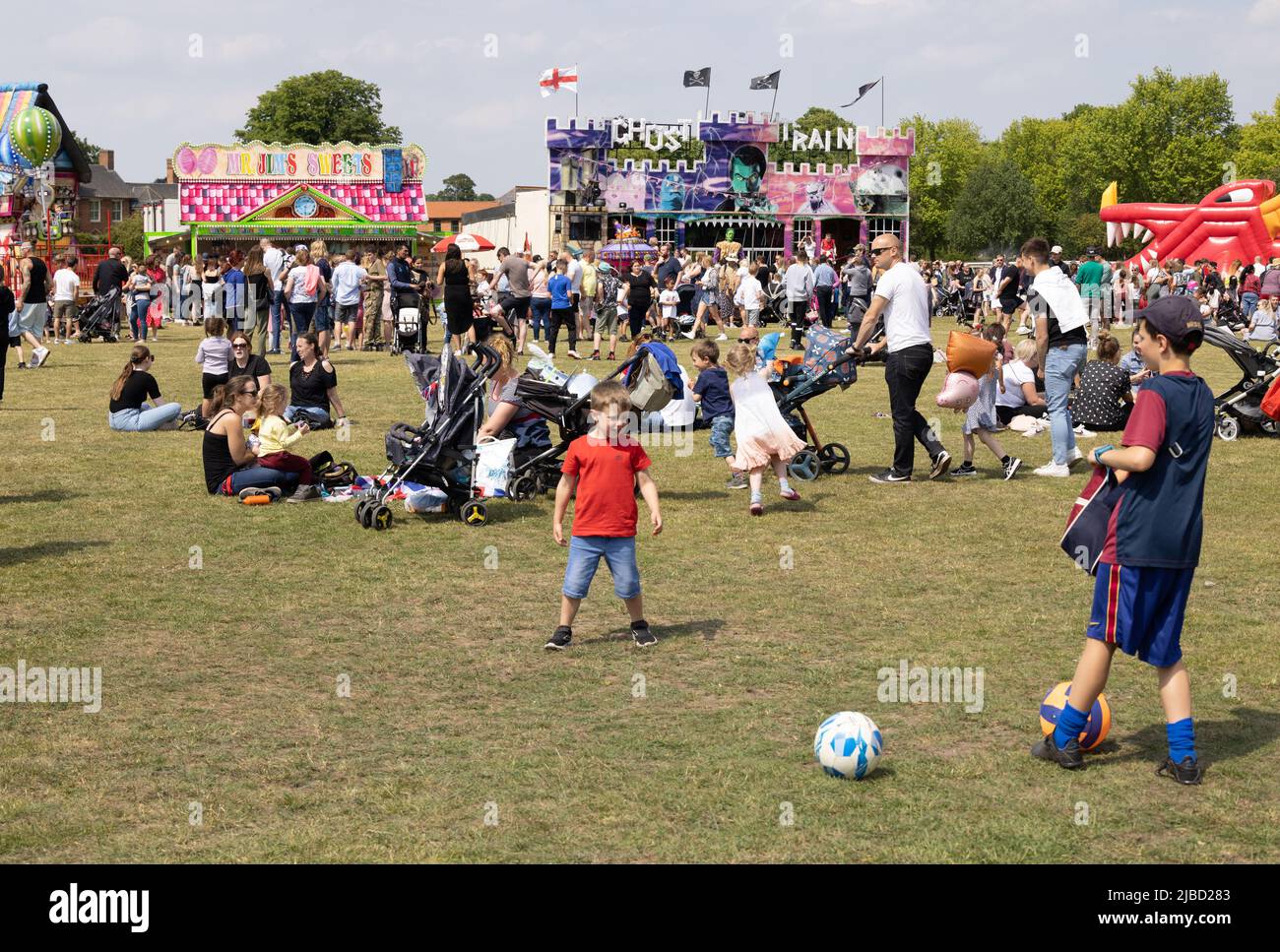 Kinder, die an einem sonnigen Feiertagswochenende im Park spielen und im Sommer eine Messe im Hintergrund haben, Newmarket, Suffolk UK Stockfoto
