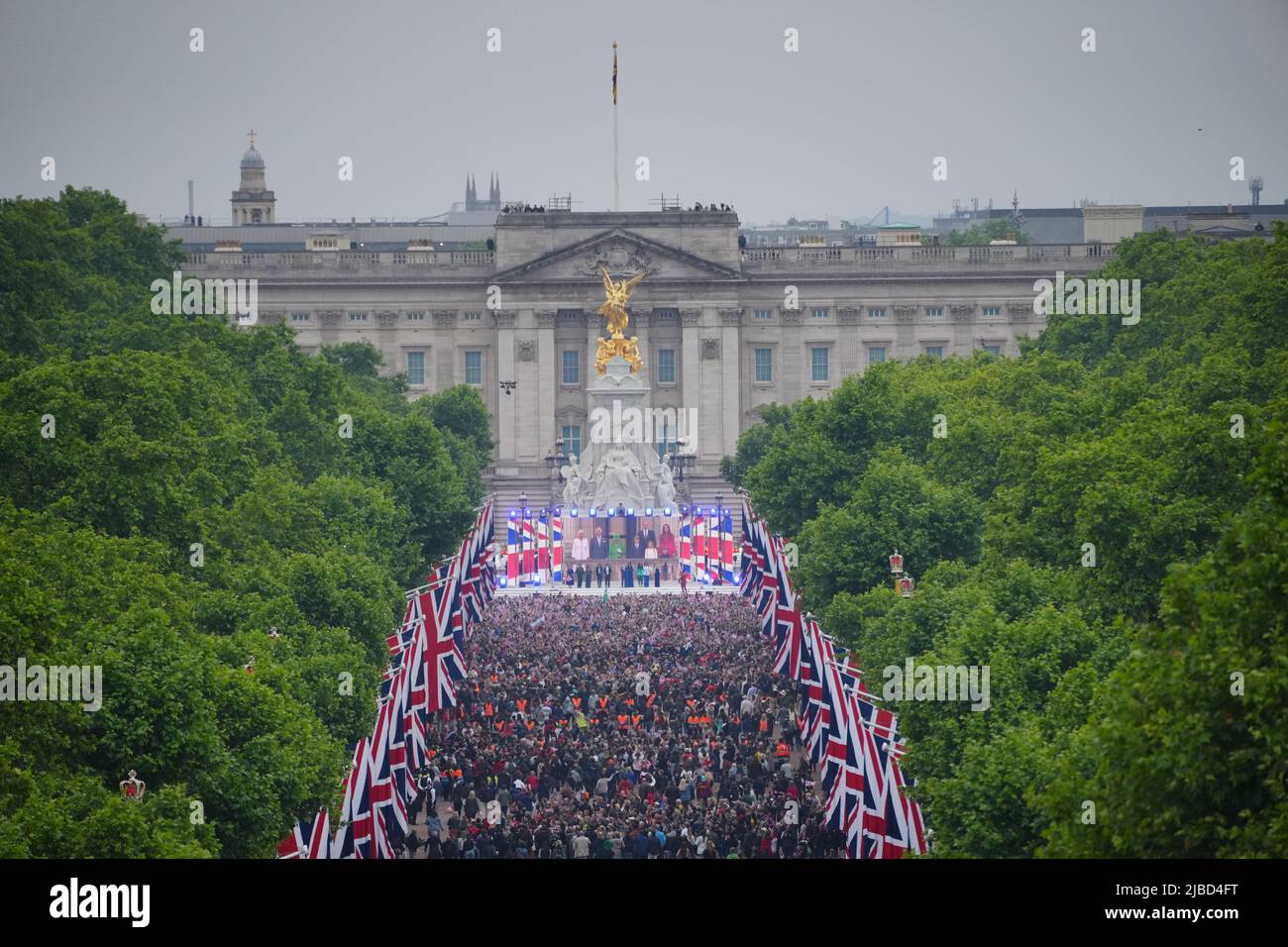 In der Mall werden Menschenmengen gesehen, wobei Königin Elizabeth II. Während des Singens der Nationalhymne auf der Platinum Jubilee Pageant vor dem Buckingham Palace, London, am vierten Tag der Platinum Jubilee-Feierlichkeiten, auf einer Leinwand gezeigt wird. Bilddatum: Sonntag, 5. Juni 2022. Stockfoto
