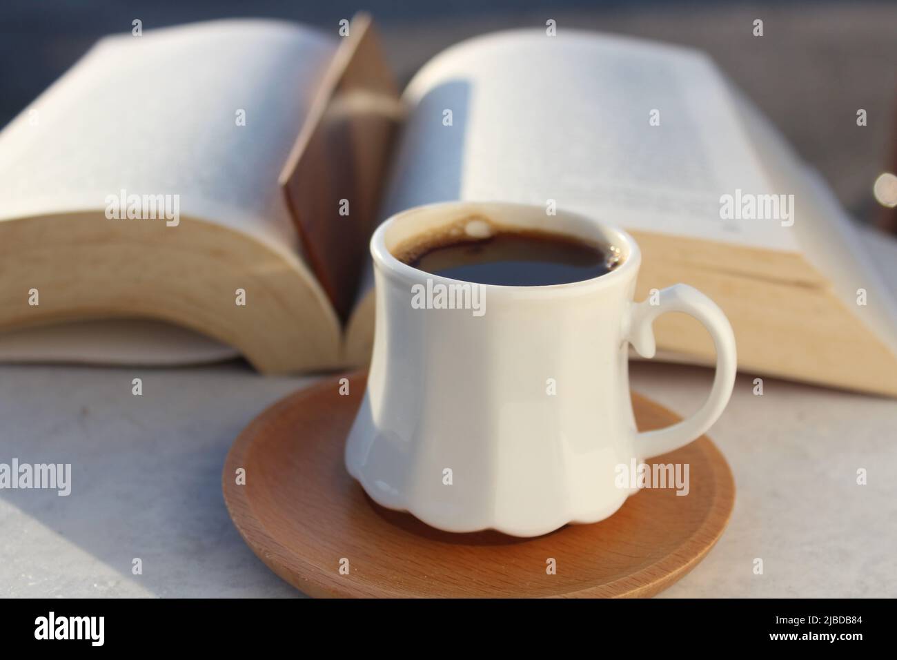 Lesebuch auf dem heimischen Balkon bei Sonnenuntergang bei einer Tasse türkischem Kaffee. Holzlesezeichen im Buch. Entspannungsstimmung, kulturelle Aktivität. Freiheit, Information, Wissenskonzept. Stockfoto