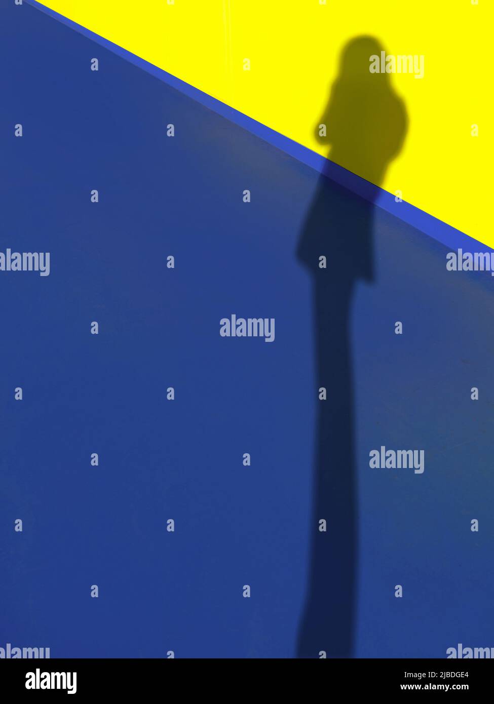 Defokussieren Sie lange Beine Schatten einer stehenden Frau auf dem leuchtend blauen Boden und der gelben Wand, sommerlich hell mit Kopierraum, abstrakte Kunst Stockfoto