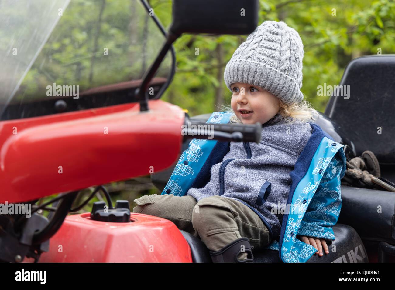 Ein ehrliches Porträt mit selektivem Fokus auf einen glücklichen, vierjährigen Jungen, der auf dem Fahrersitz eines Quad-Bikes zurückgefallen ist. Platz auf Seite kopieren. Stockfoto