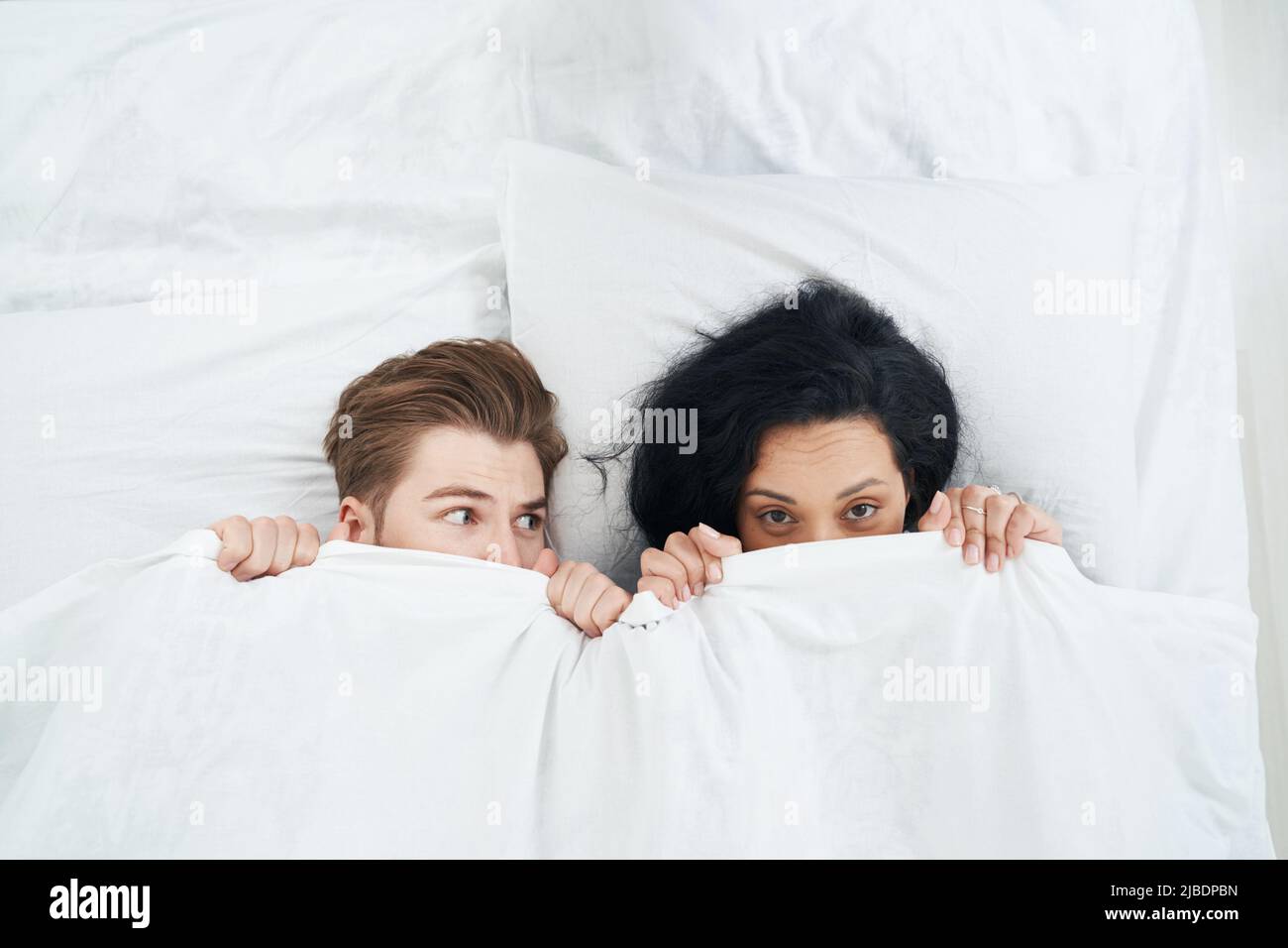 Junges Paar versteckt ihre Gesichter hinter Bettdecke Stockfoto