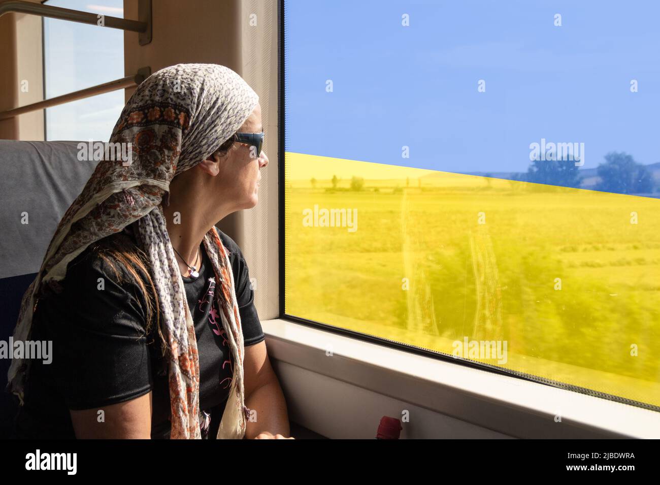 Frau, die aus dem Fenster des Zuges schaute und die Flagge der Ukraine überdeckt hatte. Ukraine, Flüchtlinge, Flüchtlinge, Häuser für die Ukraine, psychische Gesundheit, Krieg, Russland, Stockfoto