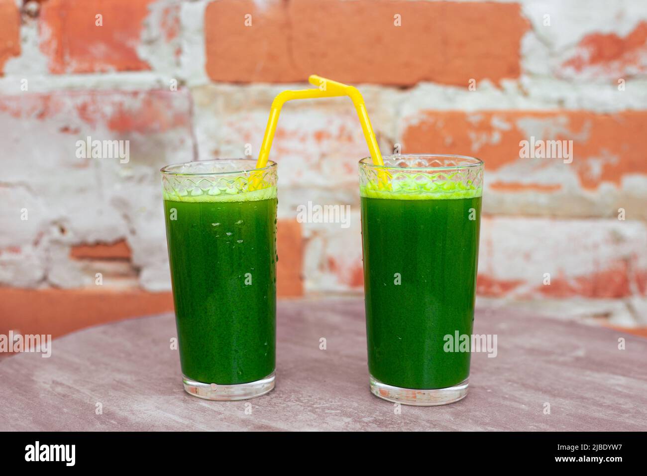 Zwei Gläser mit Getränken aus frischem Gemüse, Smoothies aus grünen Blättern, die mit Chlorophyll gesättigt sind, vor dem Hintergrund einer Ziegelwand. Gesunde Ernährung Stockfoto