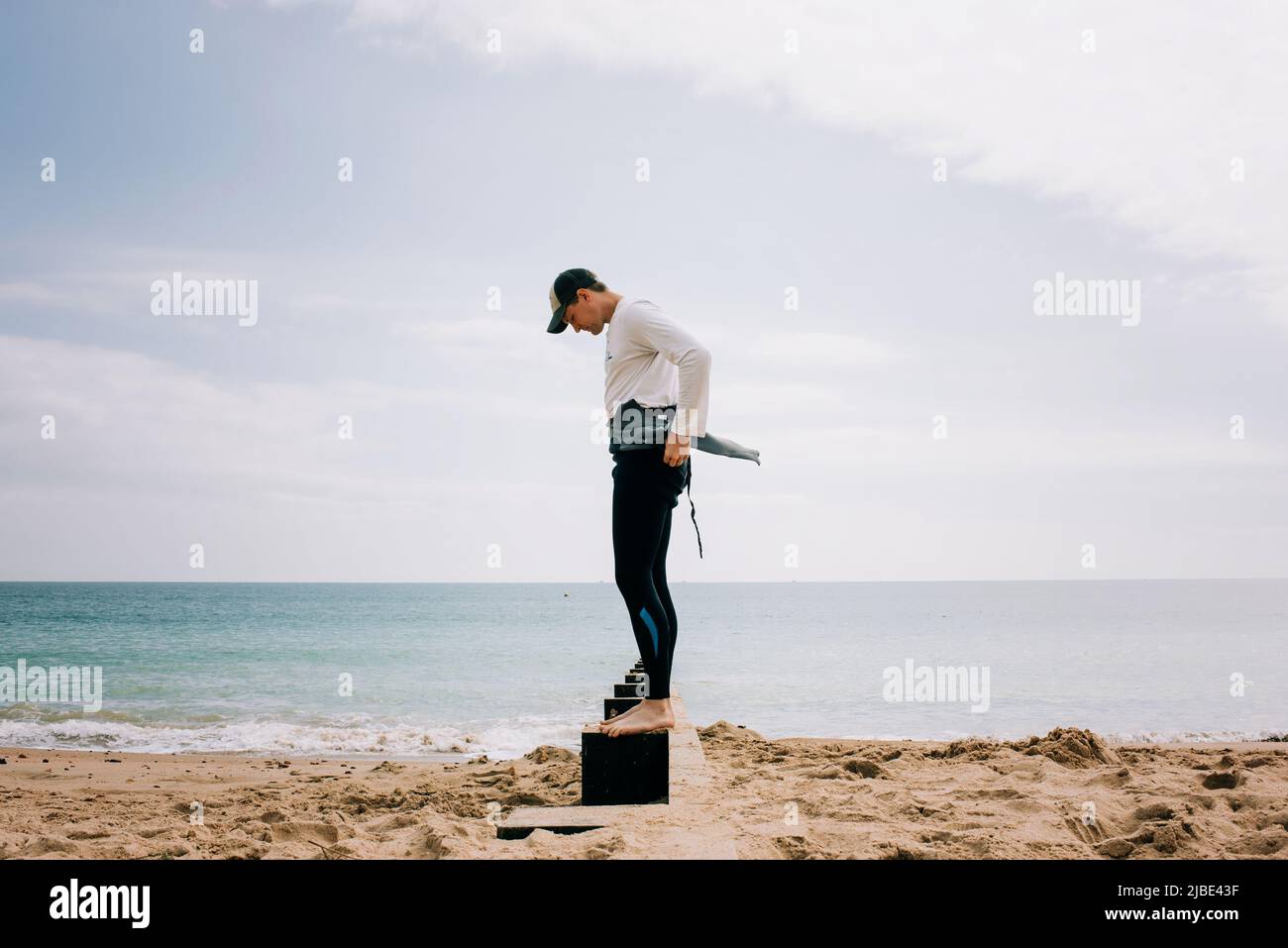 Der Mann stand auf einem Strandkiesch und zog seinen Neoprenanzug an Stockfoto