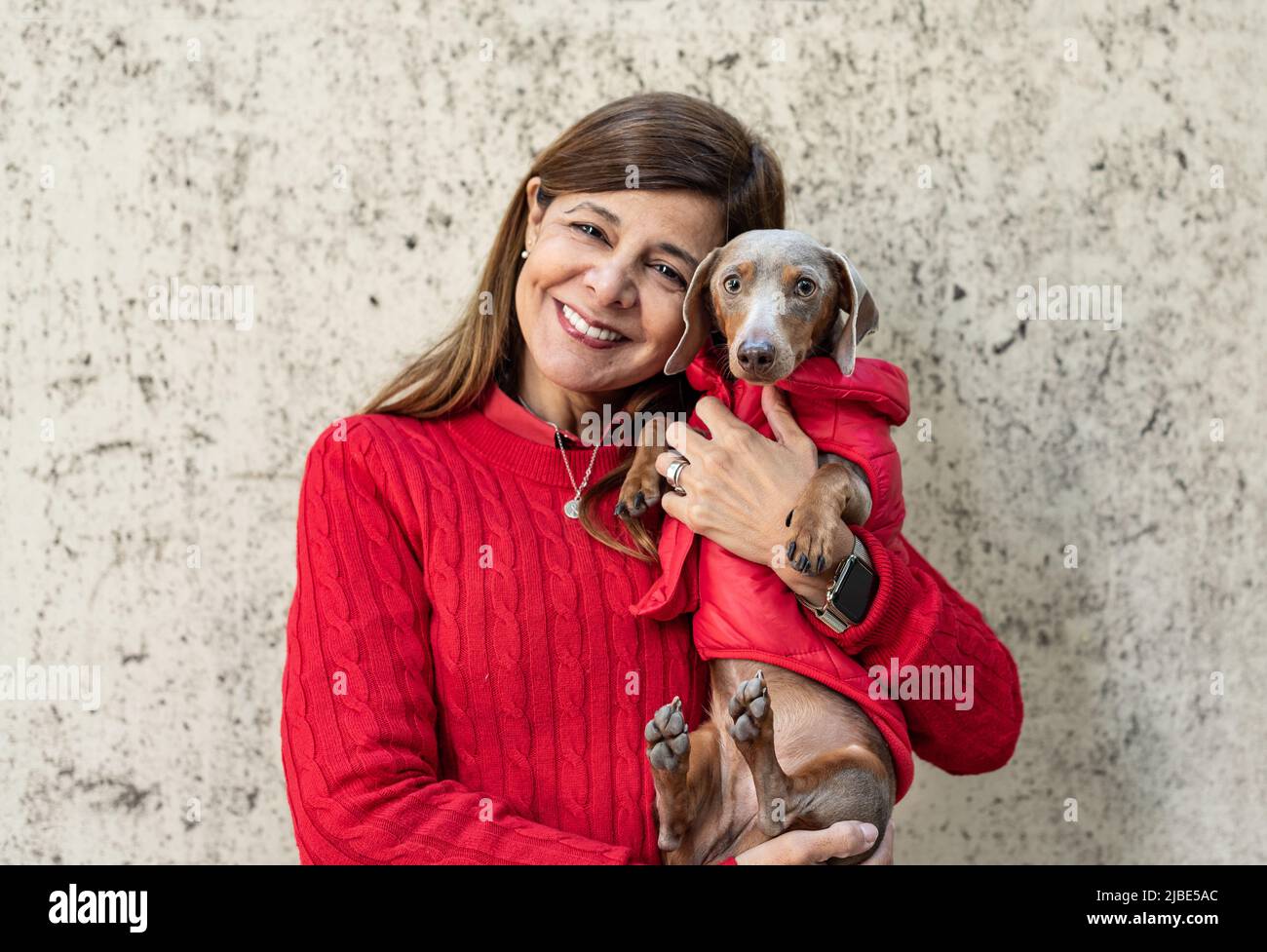Eine lateinische Frau mit ihrem Hund, beide in Rot gekleidet und in die Kamera schauend Stockfoto